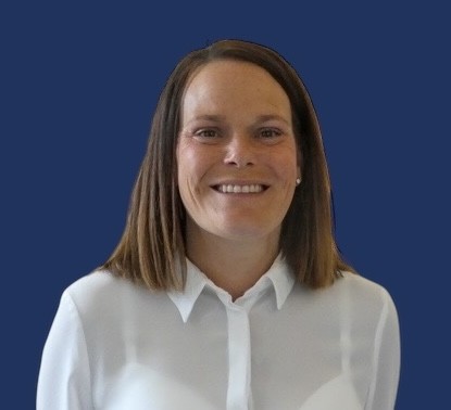 A person with straight, shoulder-length dark hair is smiling against a solid dark blue background. They are wearing a white shirt.