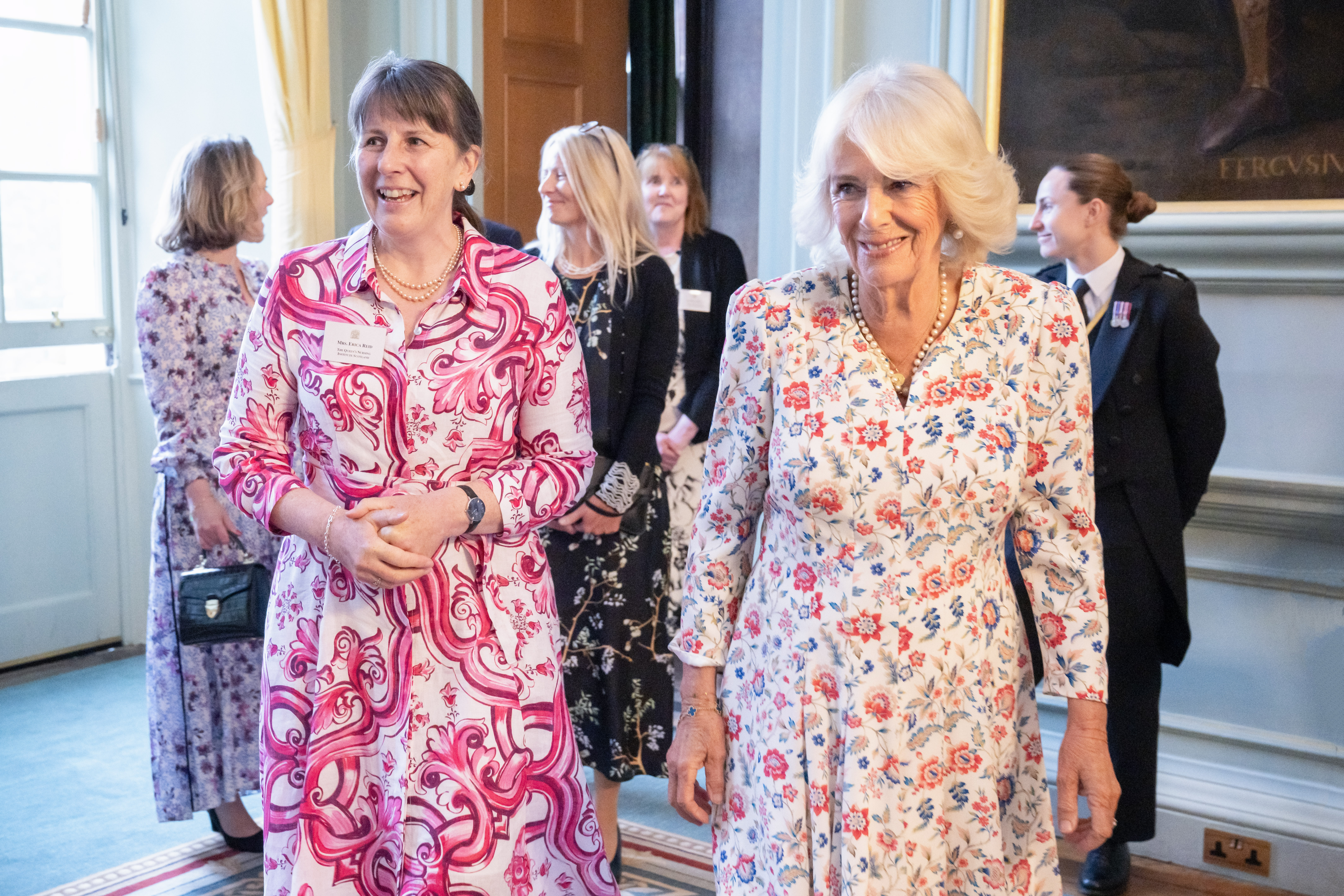 A group of people enter a room together. They are wearing smart day dress and look happy.