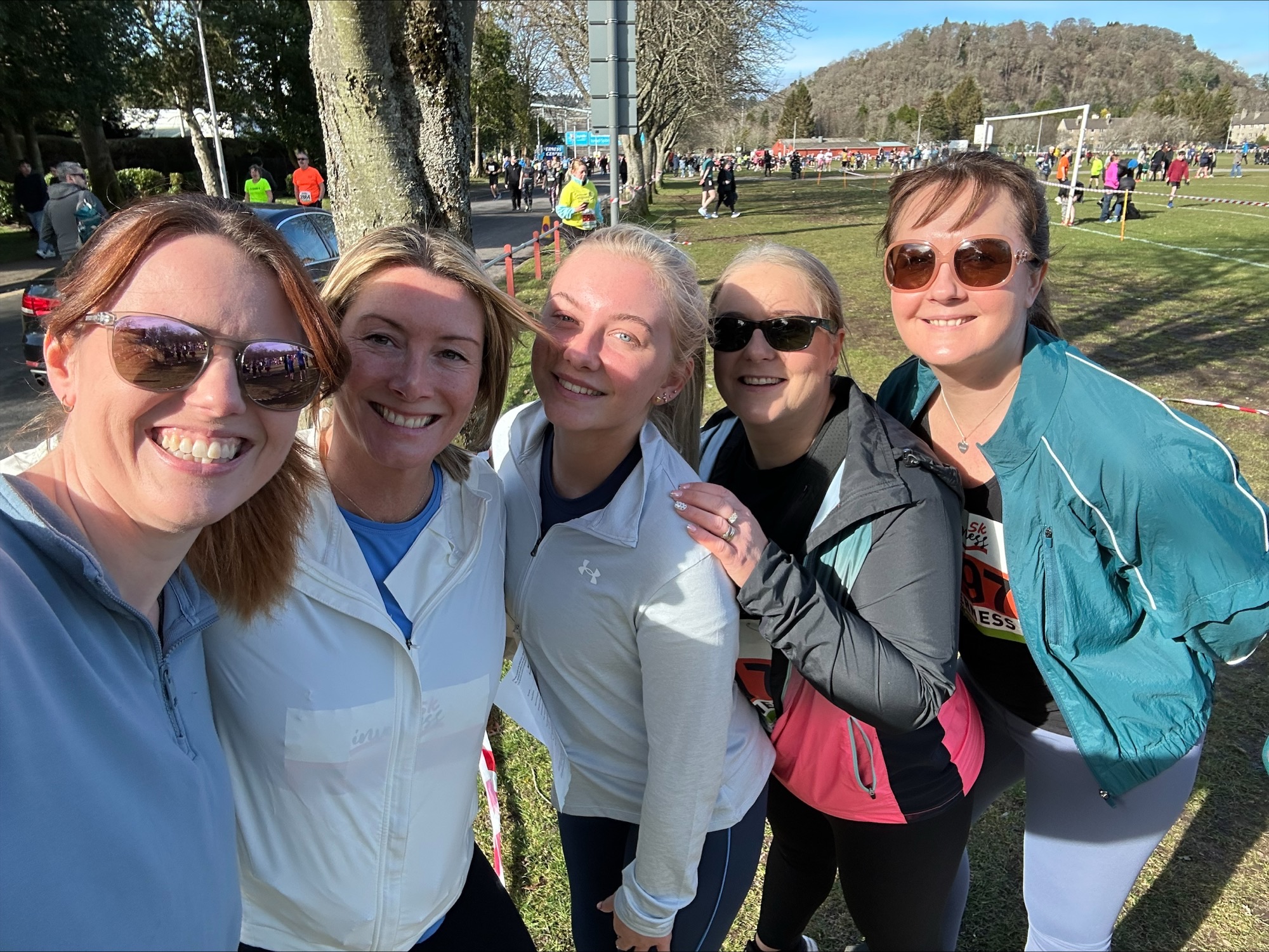 The image shows five people smiling at the camera. They are wearing active wear.