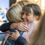 Two people hugging. The person facing forward is smiling